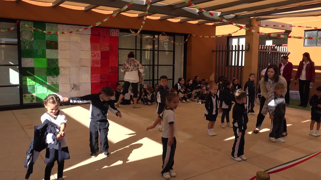 At 0:00 in San Jose del Cabo, Mexico, young children in navy and white athletic uniforms stretch in a bright courtyard as classmates and adults watch from the background.