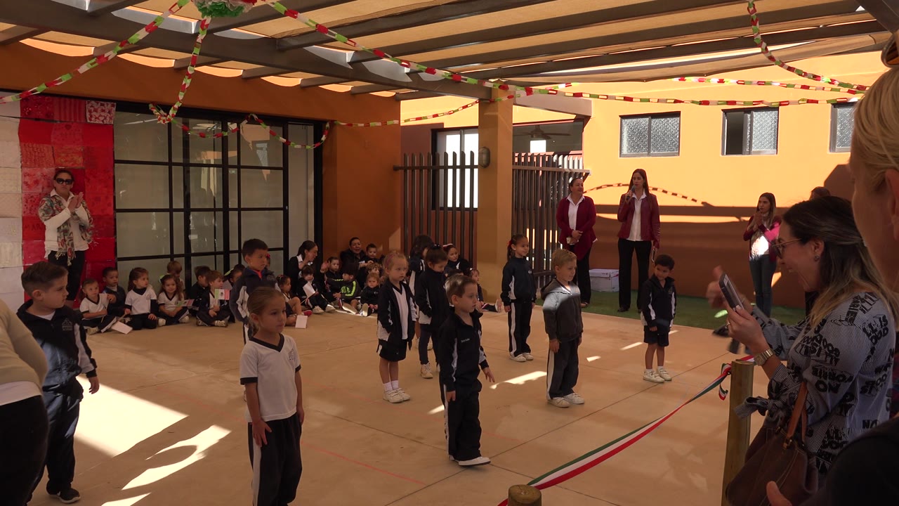A blonde spectator appears at the right edge while children stand in the courtyard.