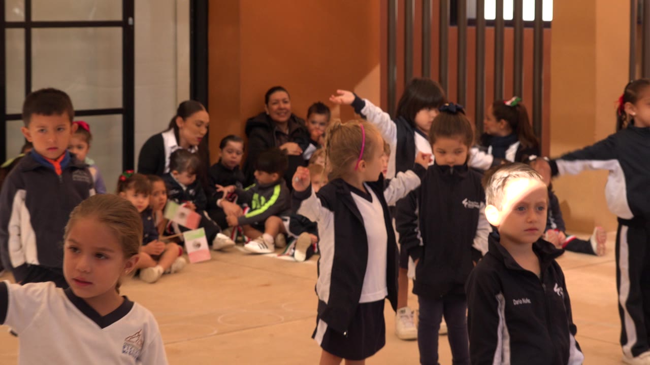 Children in navy and white uniforms gather indoors with adults behind them.