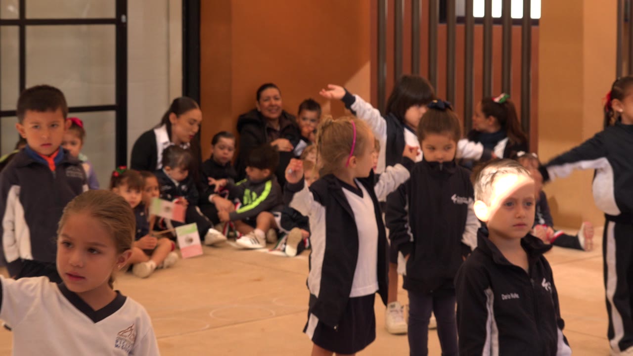 A boy faces the camera while girls in matching navy and white clothing stand nearby, with seated children and adults behind them in San Jose del Cabo, Mexico.