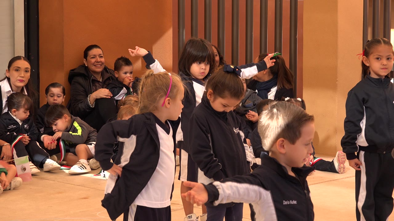 Young children in matching navy and white jackets stand close to the camera in San Jose del Cabo, Mexico, while adults and smaller children sit behind them.