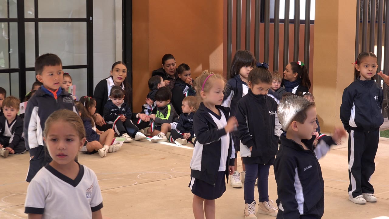 Children in sports uniforms stand and sit inside a school exercise space.