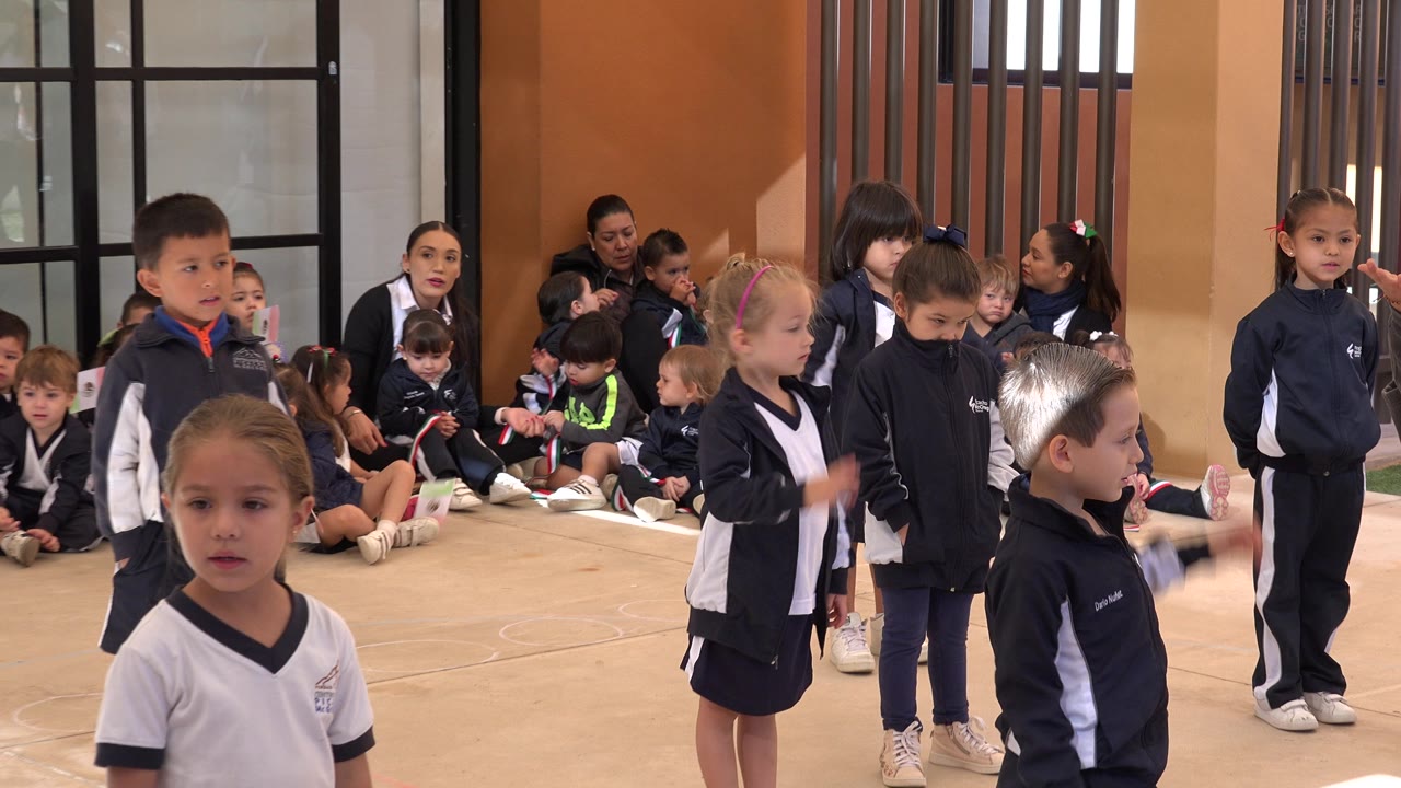 A closer view shows small children in navy tracksuits and white shirts standing before a seated group during physical education in San Jose del Cabo, Mexico.