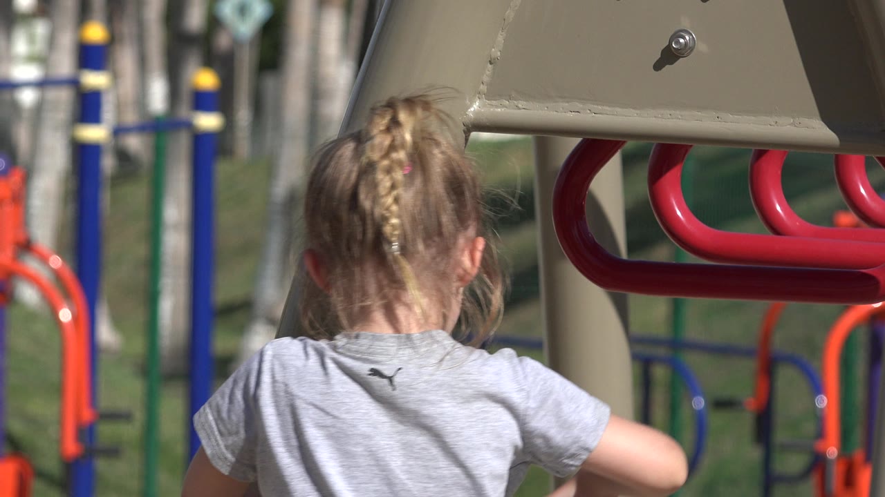 Back of a young girl under playground bars in bright sun.
