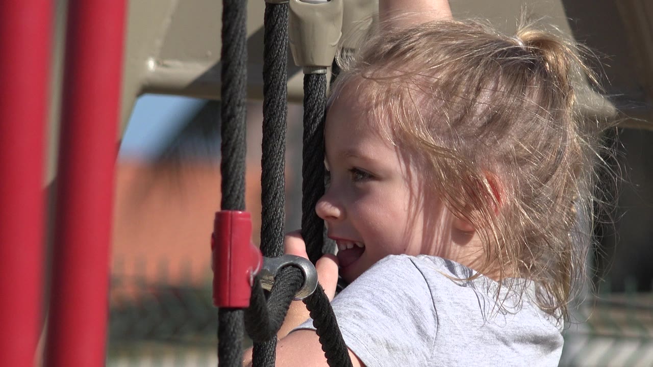 A young girl laughs near a black rope ladder and red vertical playground supports in San Jose del Cabo, Mexico.