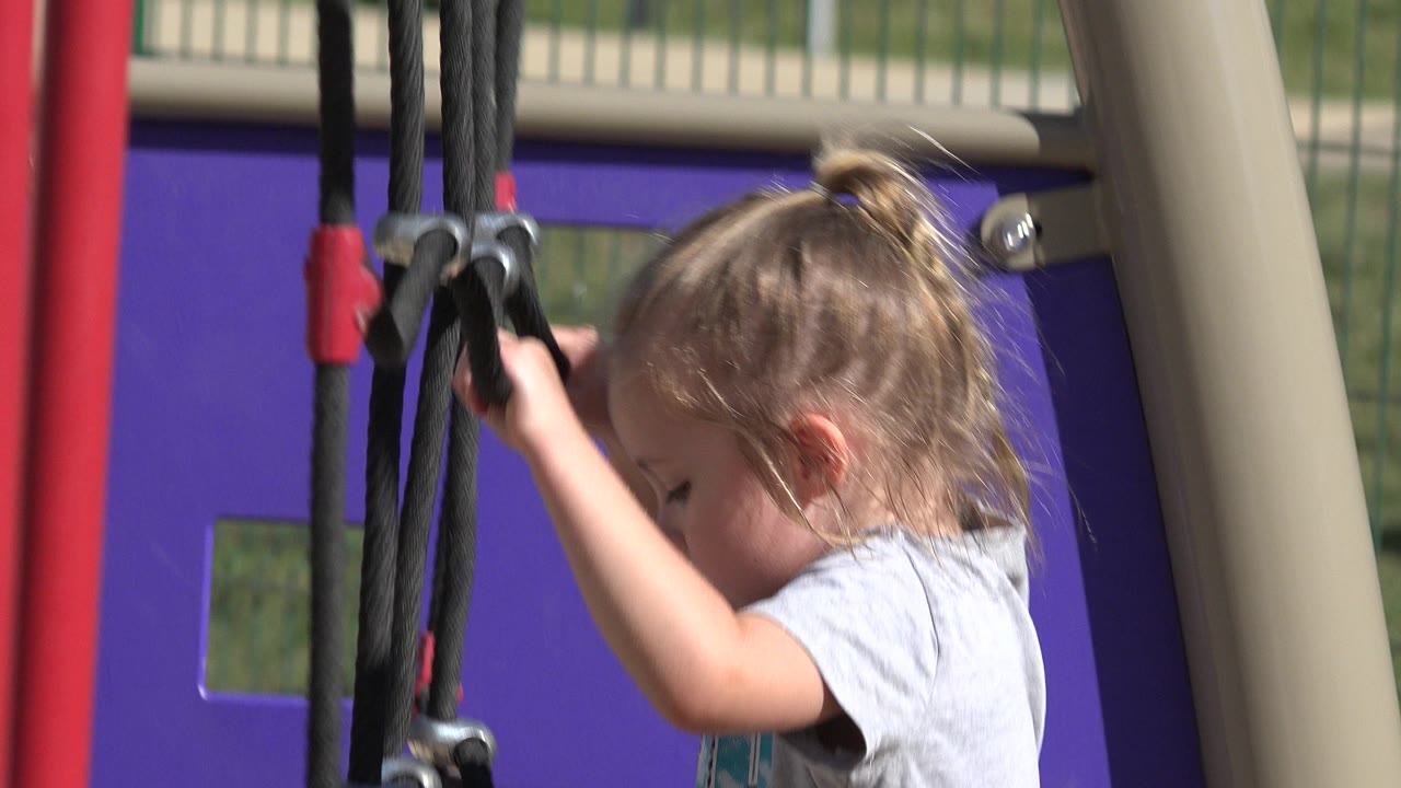 Child grips playground ropes with her face partly visible.