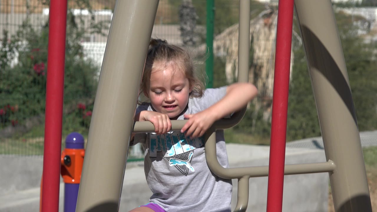 The girl remains centered on the playground equipment in San Jose del Cabo, Mexico, with one arm raised near the bar.
