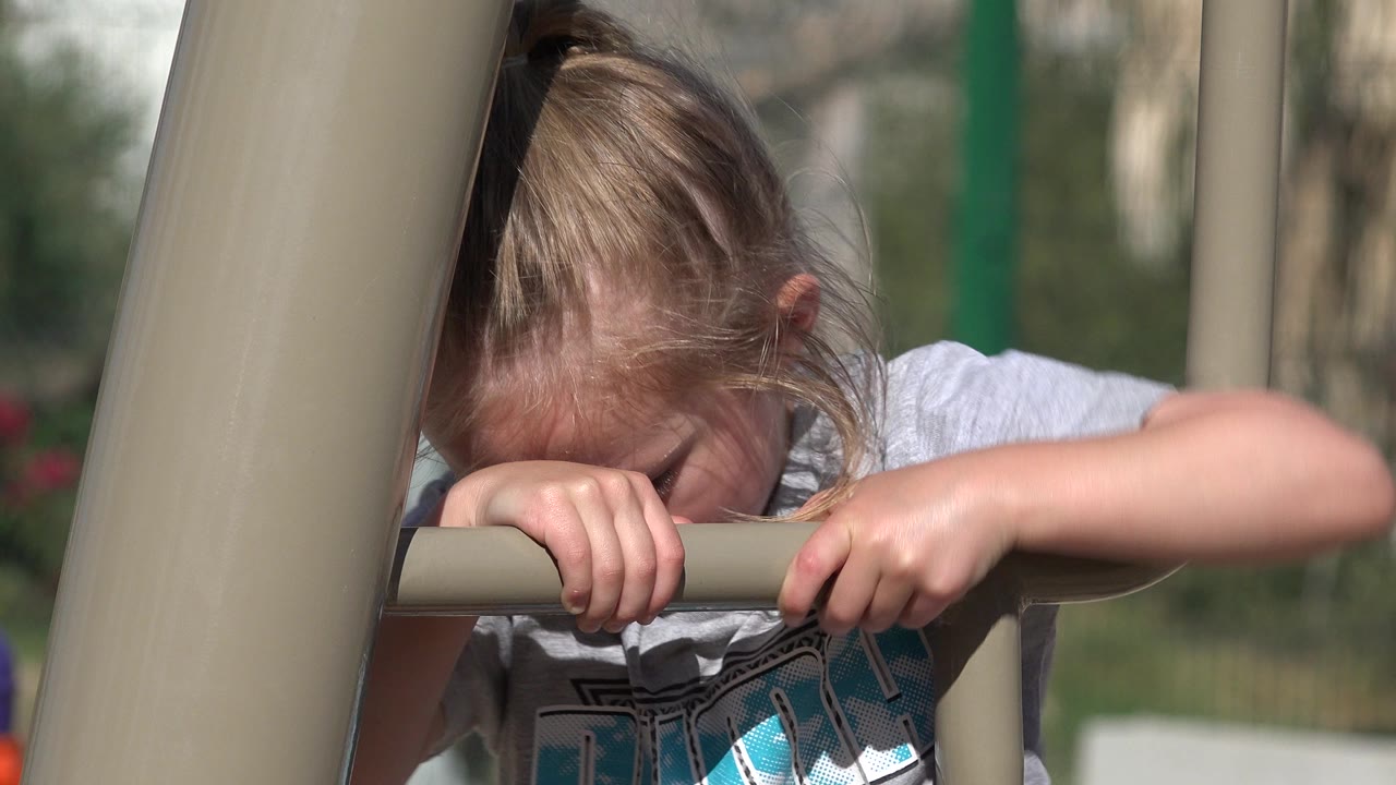 At 0:01, the blond girl remains close to the tan bar in San Jose del Cabo, Mexico, with her head lowered and one arm extended across the frame.