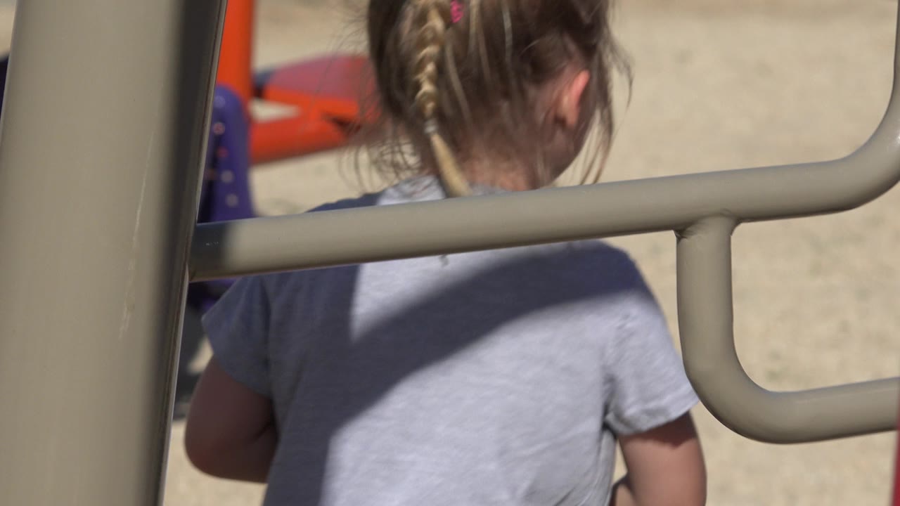 Back of a young girl seen close through playground bars.