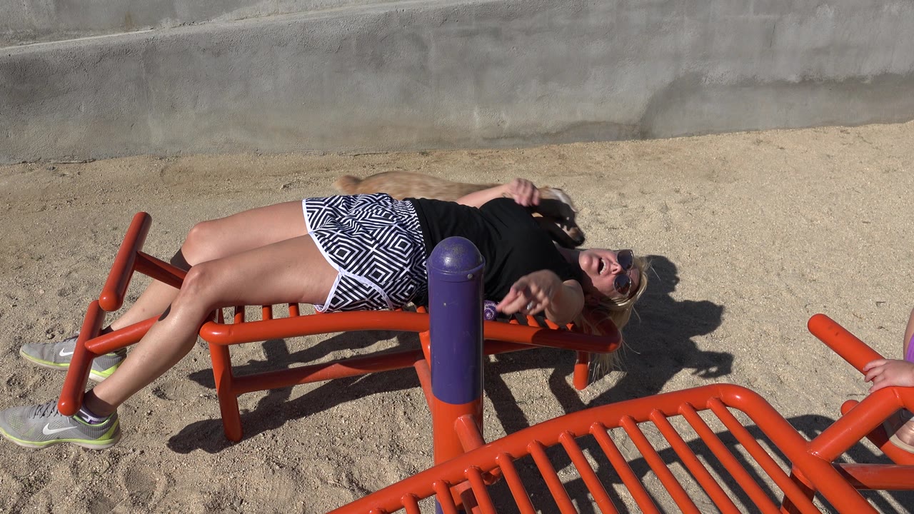 Woman in sunglasses lying on orange playground equipment in bright sun.