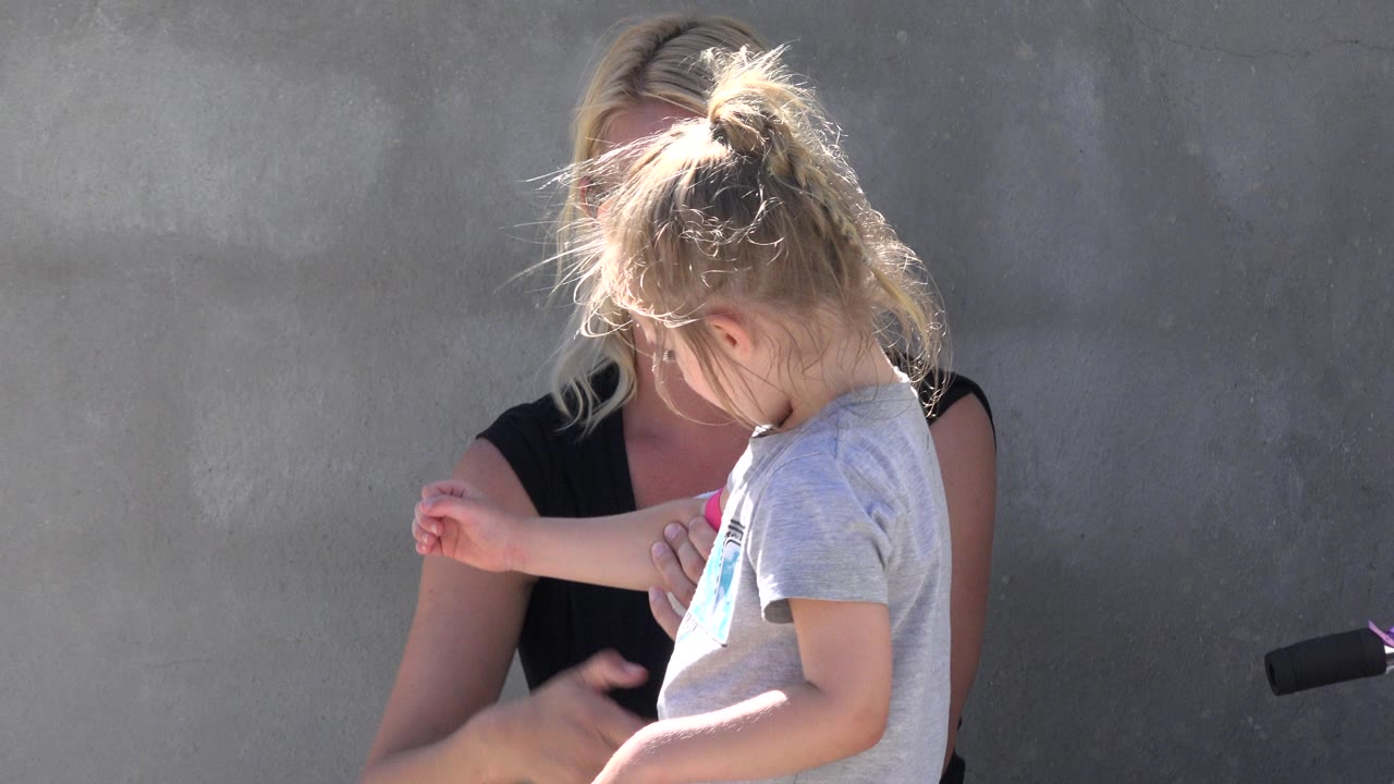 Little girl raises an arm while the woman reaches toward the elbow pad.