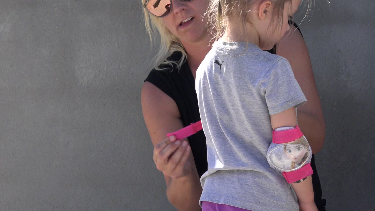 Mother faces a child while holding pink protective gear.