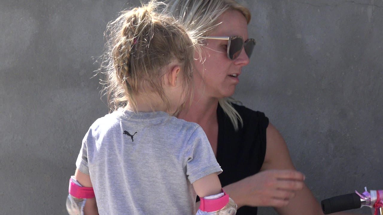 In San Jose del Cabo, the child stands with her back to camera while the adult woman looks to the side beside a handlebar-like object at frame edge.