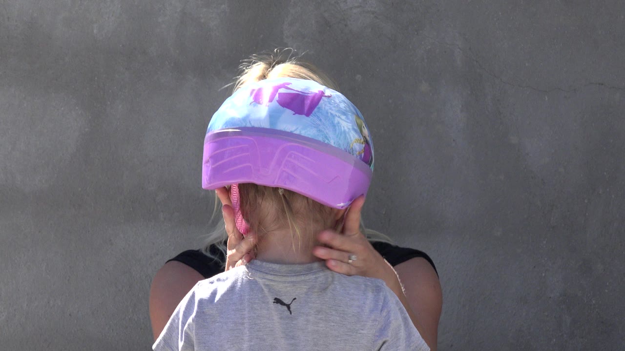 In San Jose del Cabo, the child remains turned from camera as the adult steadies the helmet and works near the pink side straps.