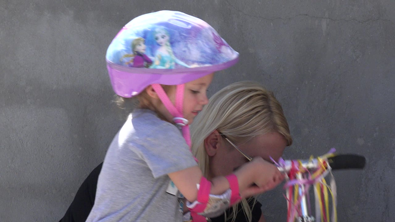 Helmeted young girl beside a scooter while an adult crouches nearby.
