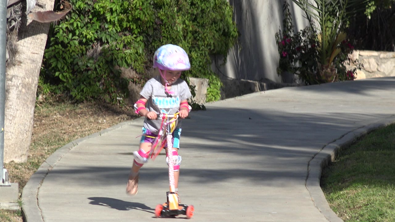 The child keeps one foot on the scooter and one foot lifted while moving along the curved walkway in San Jose del Cabo, Mexico.
