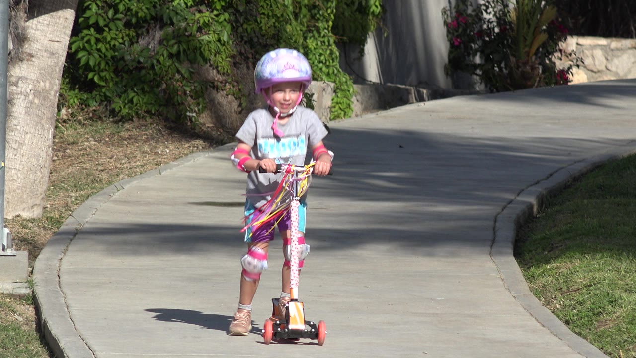Smiling child rides a scooter centered on the walkway.