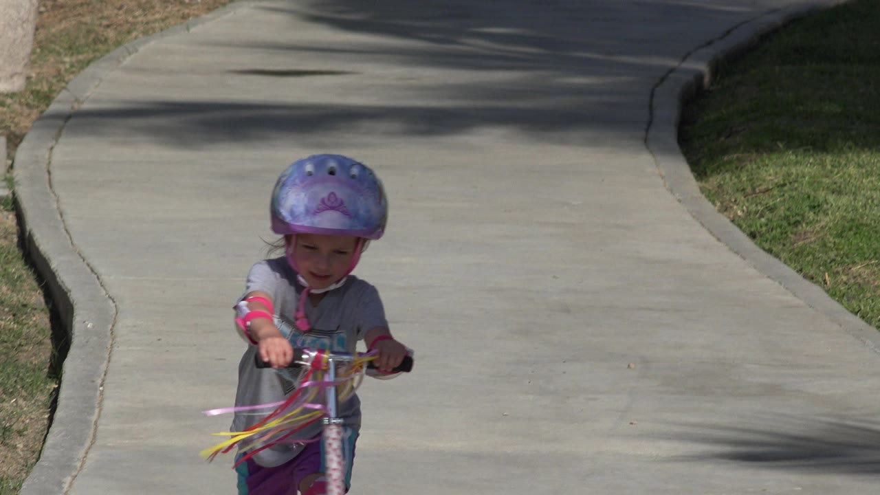 Young girl riding a scooter on a sunny sidewalk.
