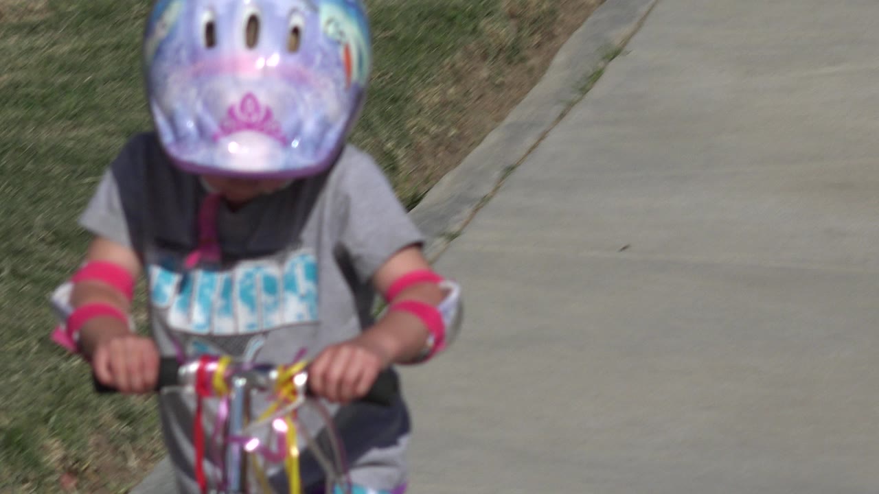 Young child in helmet riding a decorated scooter on a sidewalk.