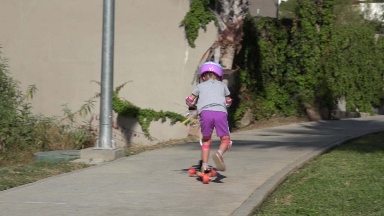 Helmeted child riding an orange three-wheeler on a concrete path.
