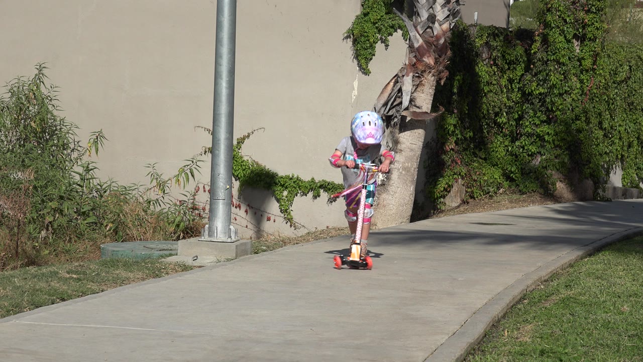 Child in helmet rides a small scooter on a paved path.