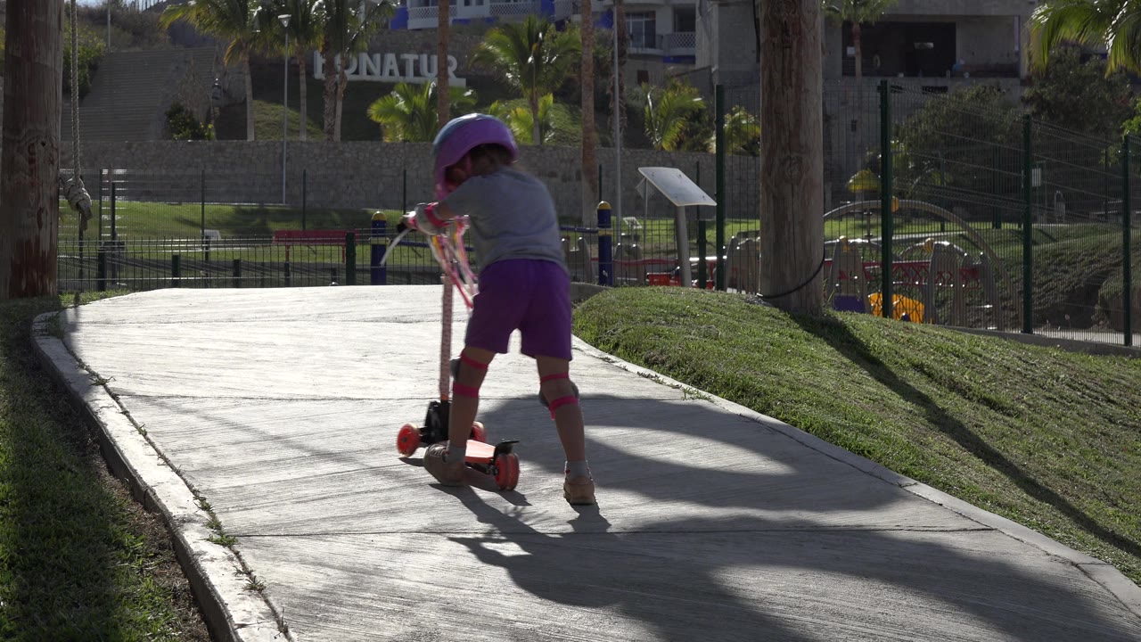 Girl turns slightly while riding a red scooter away from camera.