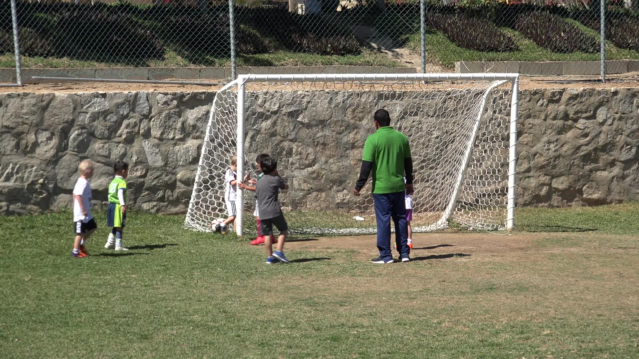 Two children stand left of the goal and another child faces the net while the adult coach watches from the right in San Jose del Cabo, Mexico.