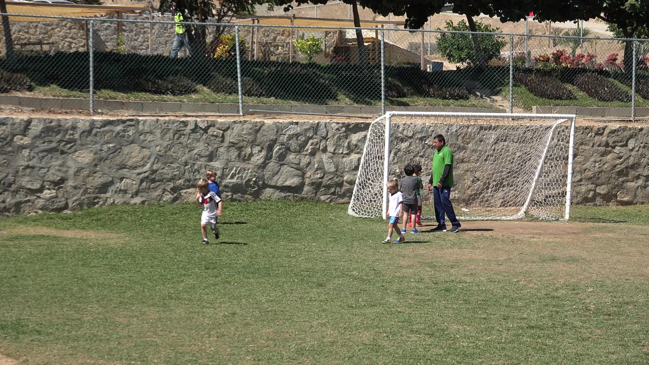 A child in white runs across the left side of the soccer field while several children and an adult remain near the white goal in San Jose del Cabo, Mexico.