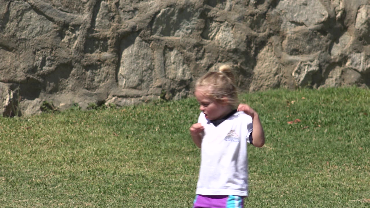 Blonde child running on grass beside a stone wall