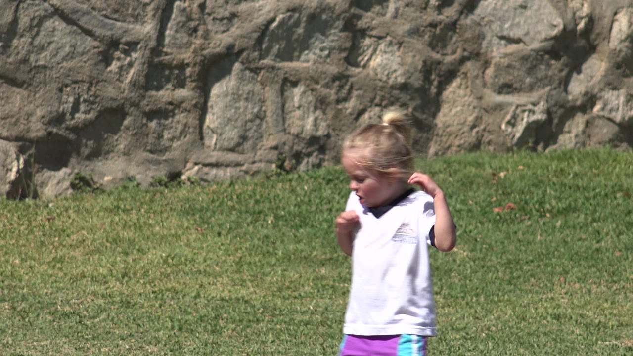 The same child continues across the sunny grass field in San Jose del Cabo, Mexico, with the textured stone wall filling the background.