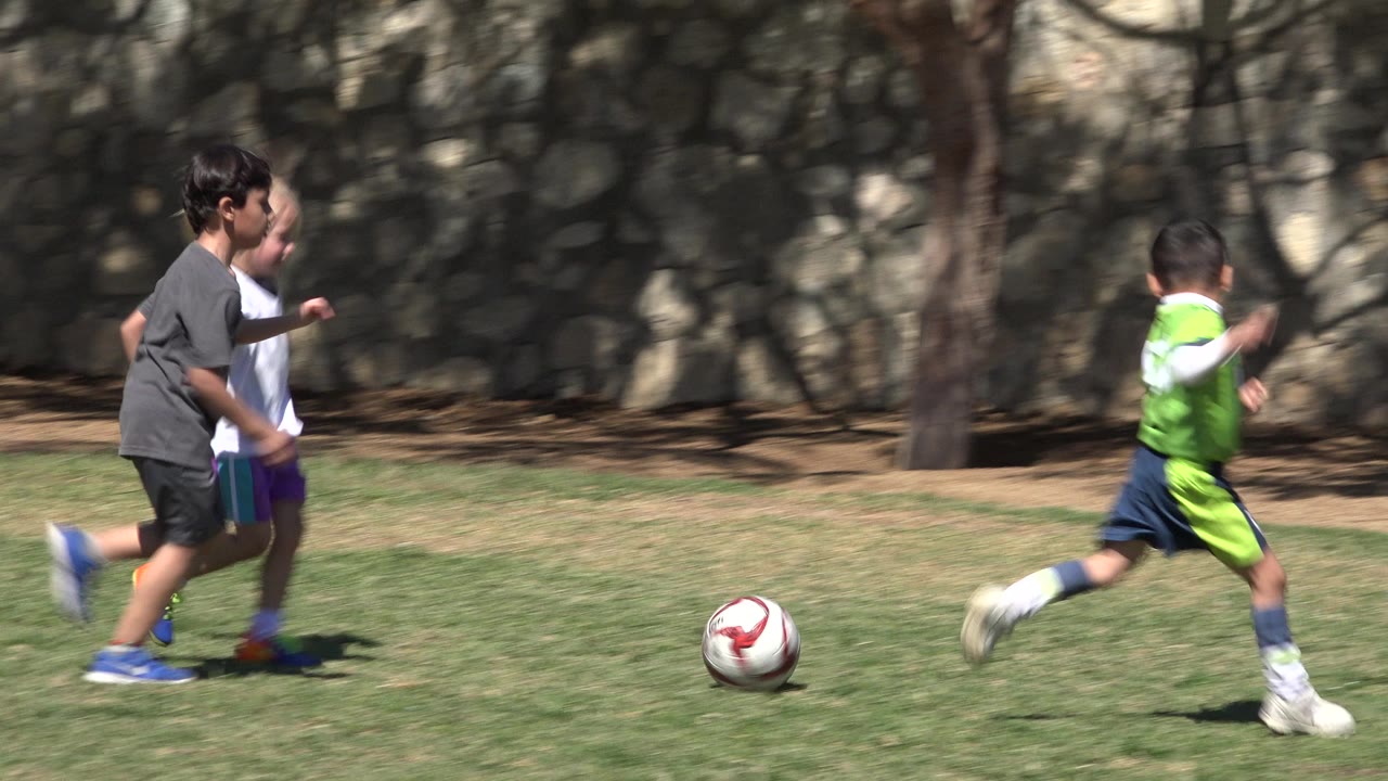 Children run on grass near a red and white soccer ball.