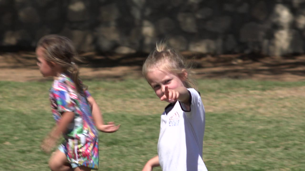 Girl points toward the camera as another child runs past.