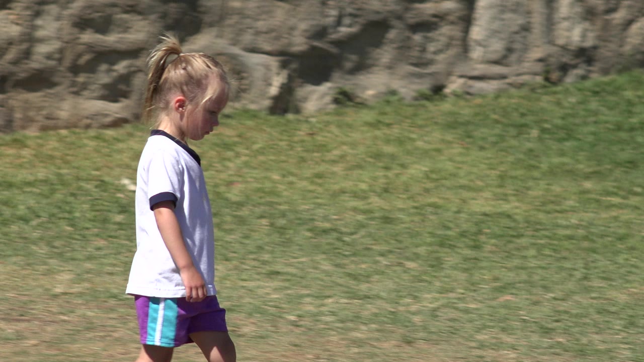 The girl remains in profile in San Jose del Cabo, Mexico, walking across sunlit grass with the rocky wall filling the background.