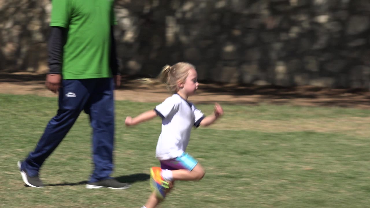 Young child running on grass beside a partial adult.