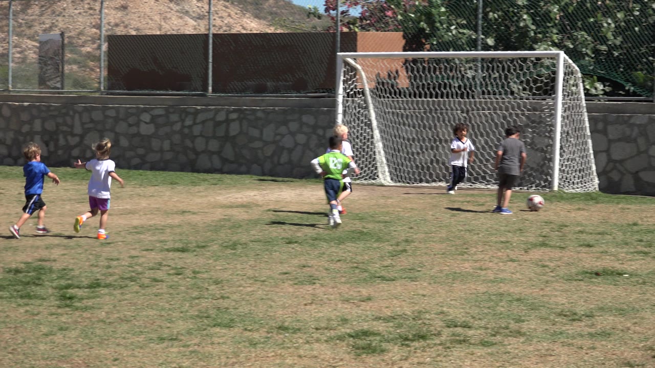 Children continue toward the soccer goal in San Jose del Cabo, Mexico, as a child in gray moves with the ball near the right side of the frame.