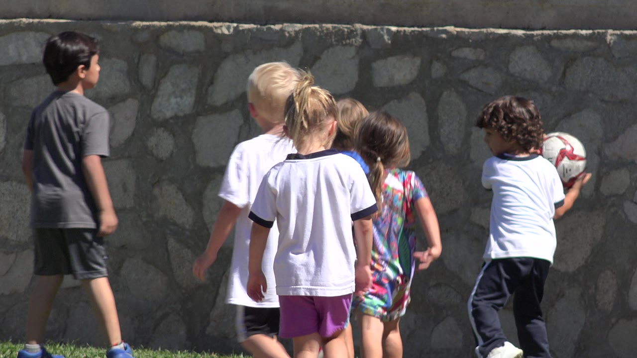 Children walking with a soccer ball near a wall