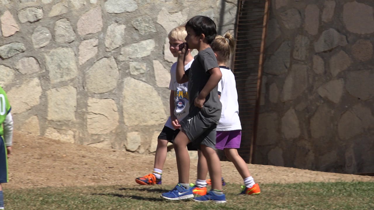 Three children pass the same stone wall in San Jose Del Cabo, Mexico, with bright shoes and casual sports clothing visible.