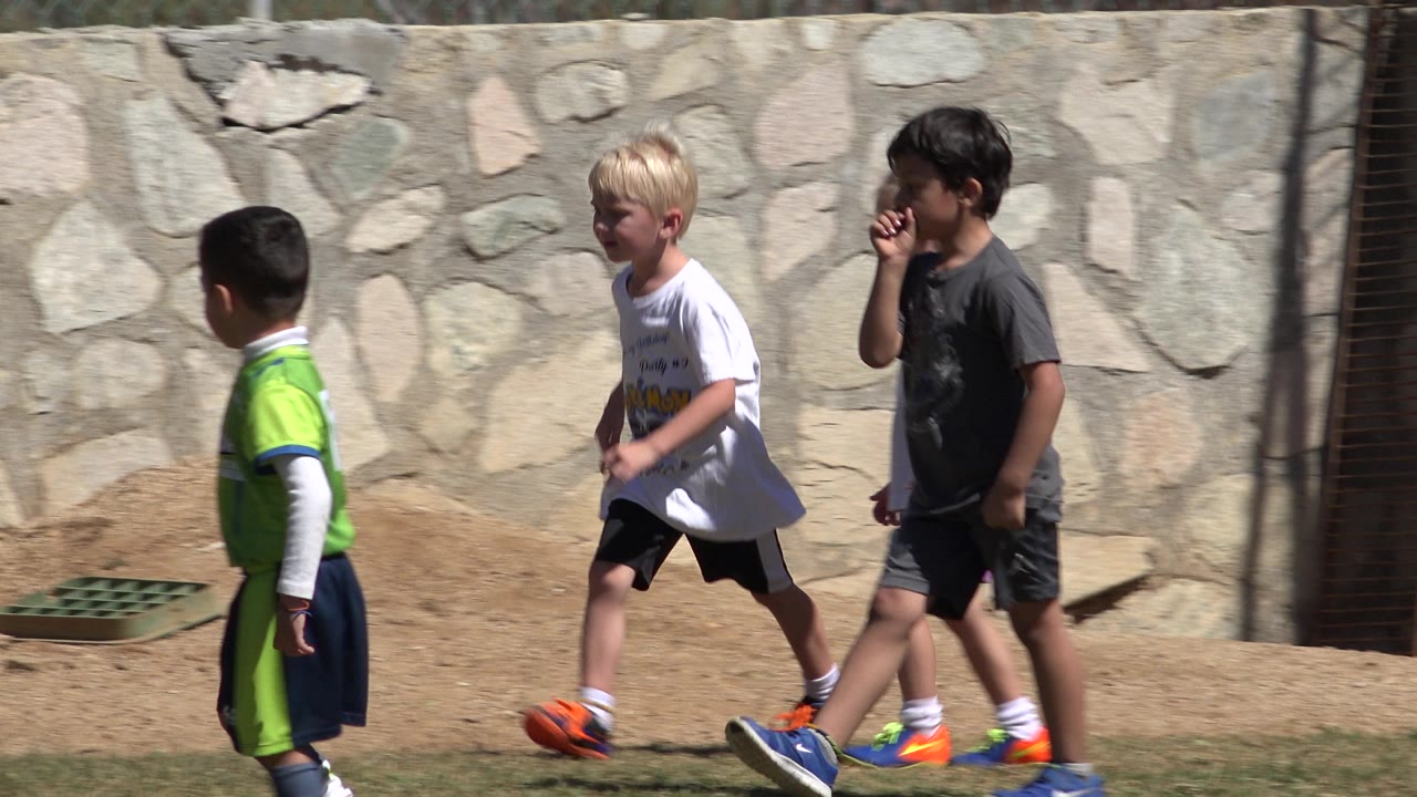 Children run and walk past a stone wall.