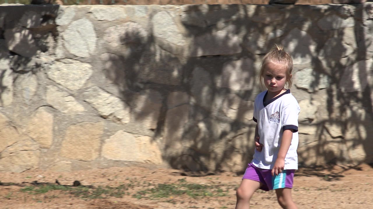 Blond child walking barefoot beside a stone wall.