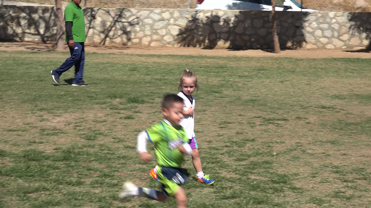 Boy runs in front of a girl on a grass field.