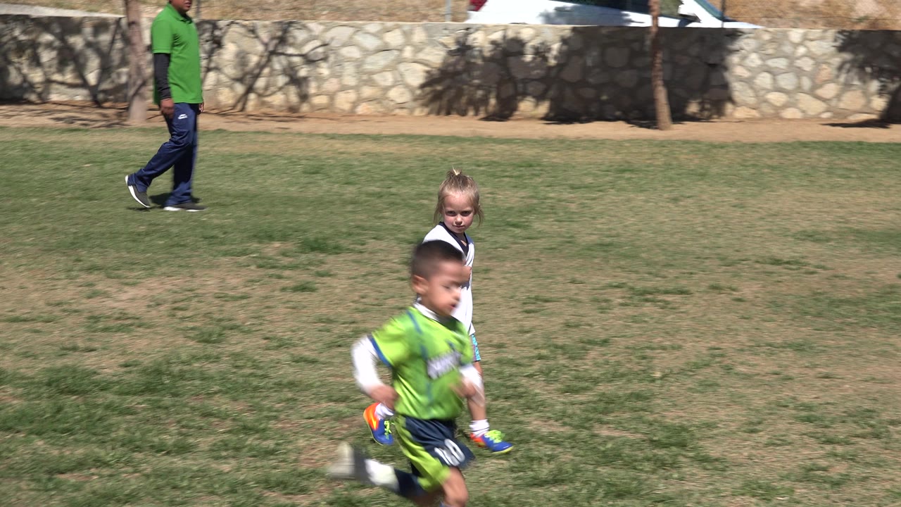 The boy continues moving across the foreground in San Jose Del Cabo, Mexico, with the girl in a white sports shirt behind him and an adult walking near the stone wall.