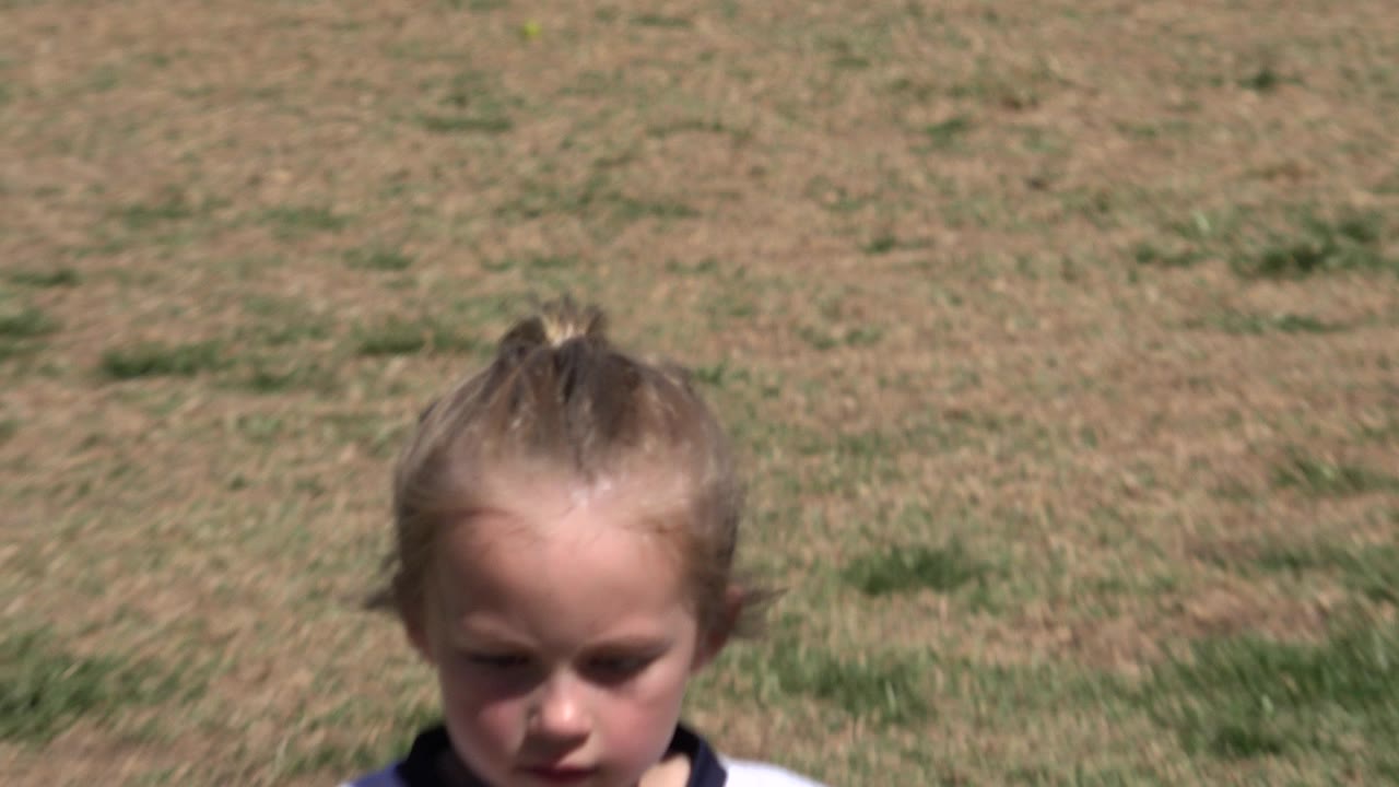 The girl remains close to the lens with her face partly shaded while the dry, patchy soccer field fills the background in San Jose del Cabo, Mexico.