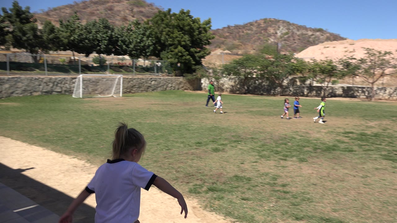 Girl in foreground near a soccer field with children in the distance.