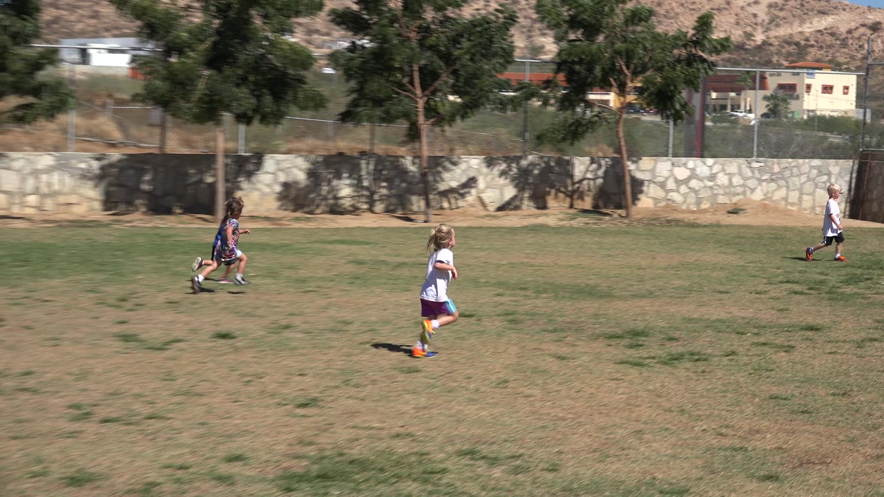 Wide field frame in San Jose del Cabo, Mexico, with a blonde child in a white shirt running in the foreground and other children farther back near the stone wall.