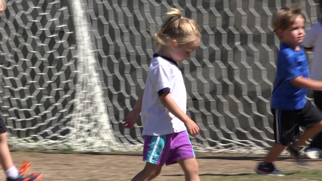 A boy in a blue shirt runs across the field in San Jose del Cabo, Mexico, while the girl in a white jersey passes near the goal net.