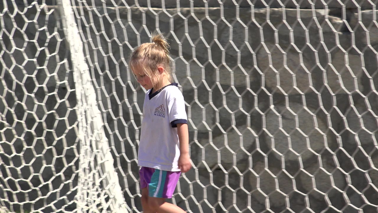 Young girl walking beside a white soccer goal net.