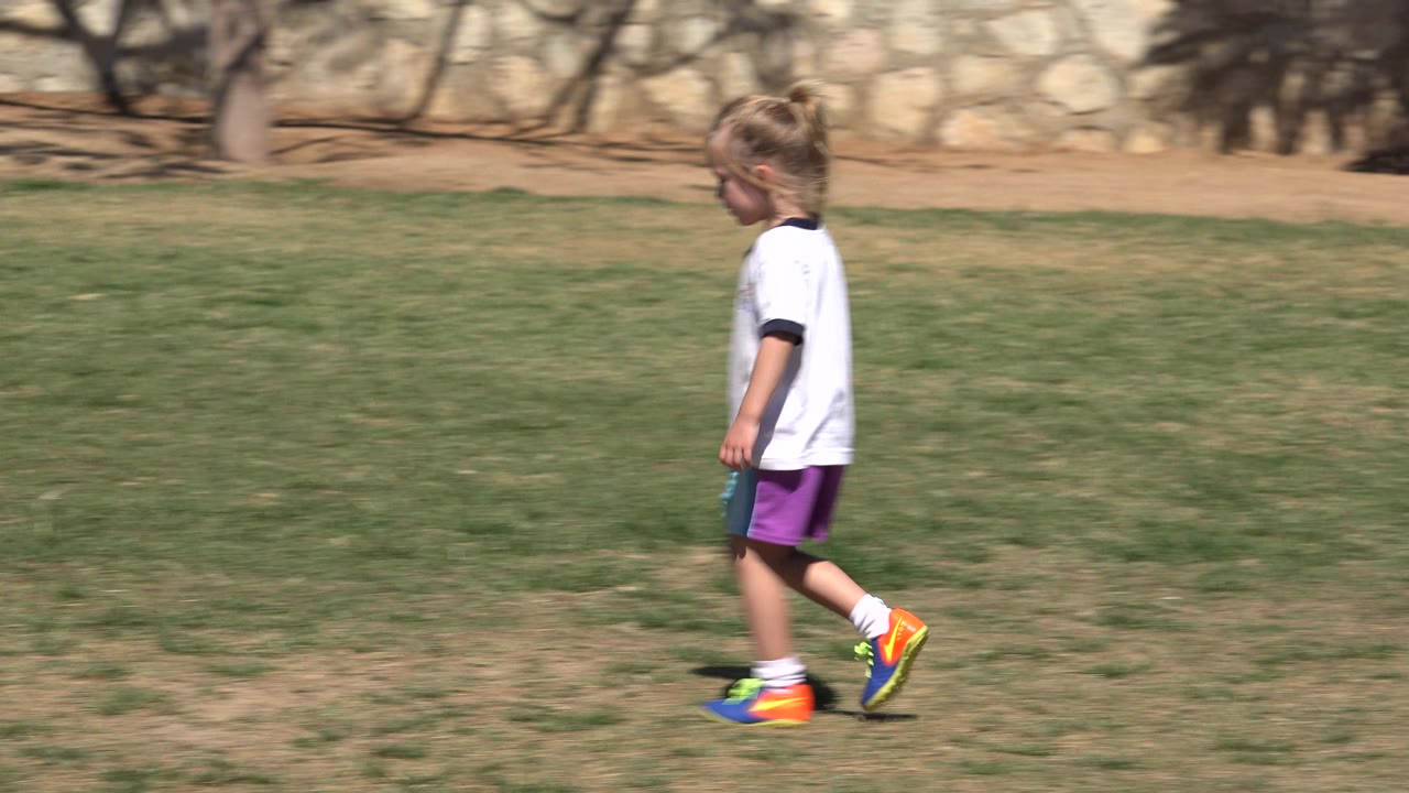 Young girl walking on grass with more open field ahead of her.