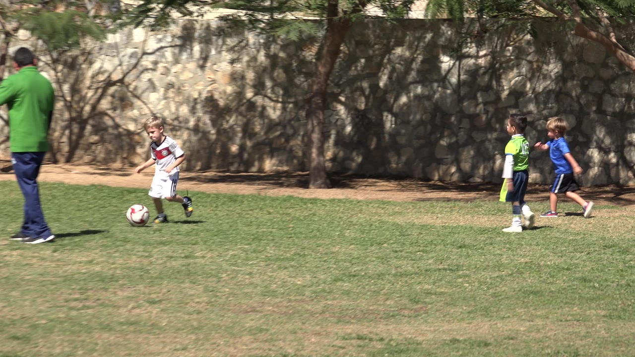 Children and an adult stand and walk on a grassy soccer field.