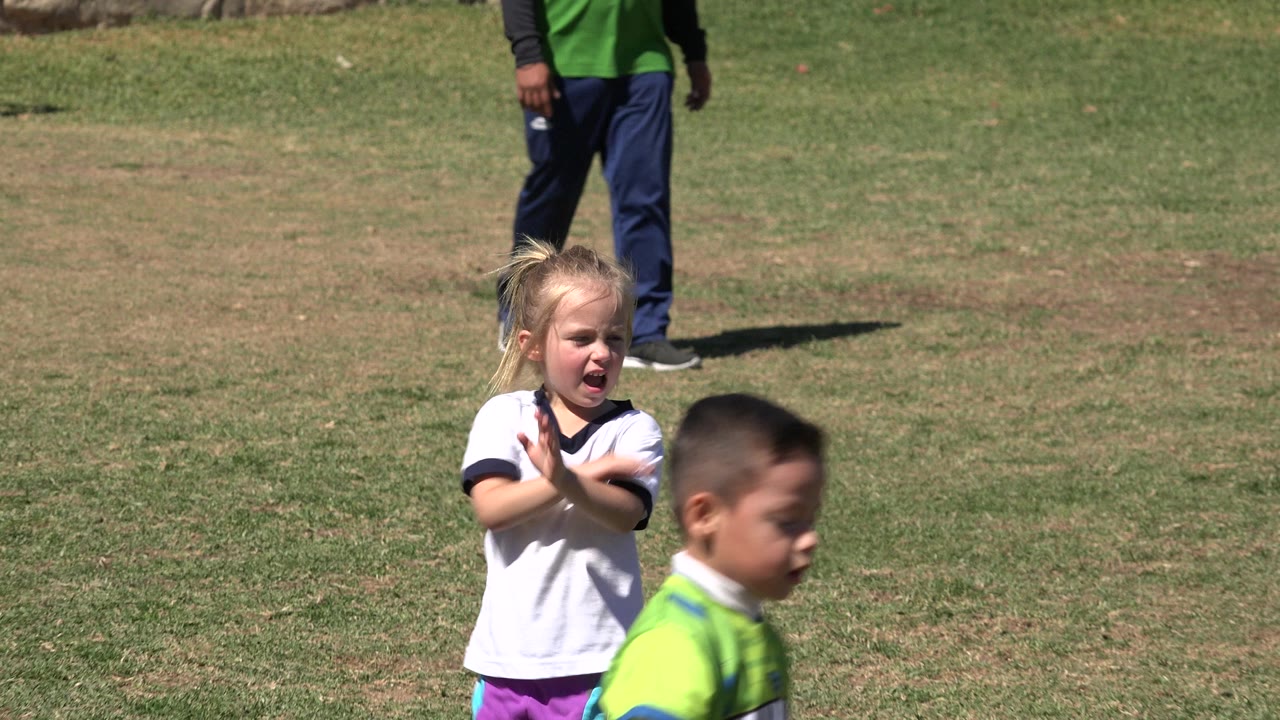 At 0:01 in San Jose del Cabo, Mexico, the girl remains near center with her arms raised while the boy in a green vest passes closer across the lower right foreground.