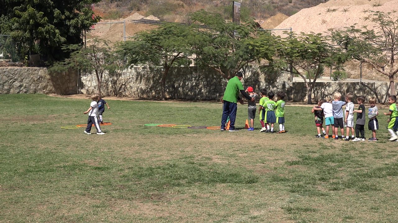 Children and a coach on a grassy field with colored hoops.